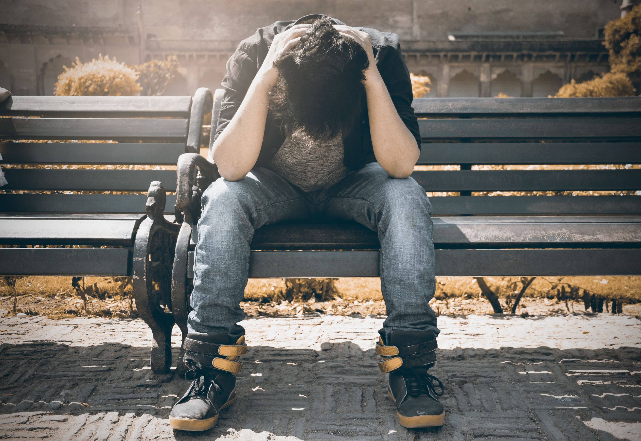 Man in black shirt and gray denim pants sitting on gray bench