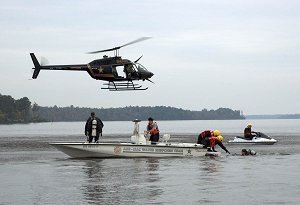 A helicopter hovers over 2 search and rescue boats.